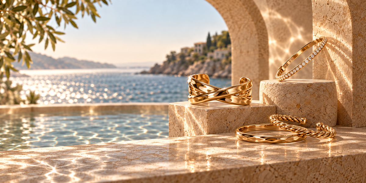 Layered gold bracelets on curved travertine monoliths beside a Mediterranean coastal view